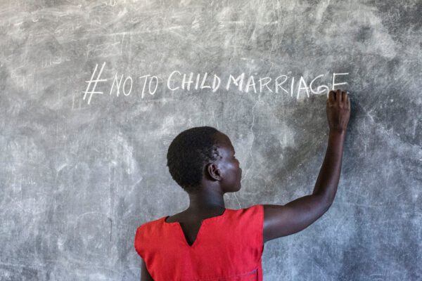 Rygg på en ung kvinna framför en svart tavla där det står # No childmarriage