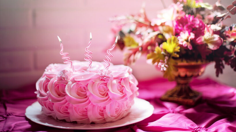 rosa tårta med tre rosa ljus framför blombukett i vas, foto