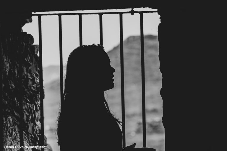 kvinna i motljus framför ett fönster med galler