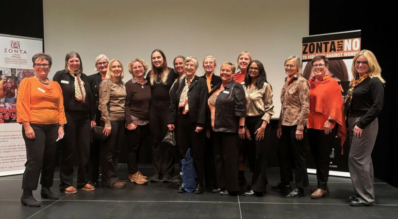 En gruppbild på glada kvinnor på en scen. Snett bakom gruppen står ett par skylt med synlig text. Den ena texten lyder: Zonta Club of Värnamo. Den andra: Zonta says no to violence against women