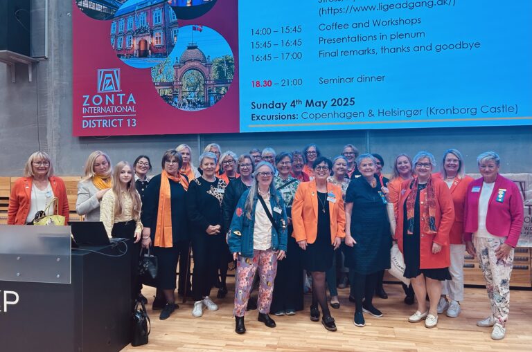 Samling kvinnor på en scen med en bildpresentation i bakgrunden.