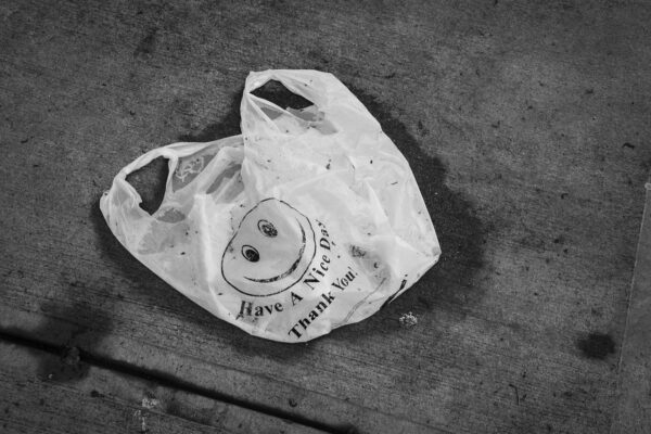 En vit plastpåse tillplattad på asfalten. Plastpåsen har en smiley med följande text: Have A Nice Day Thank You.