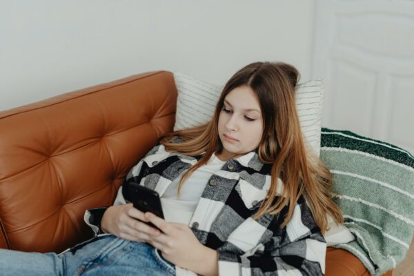 Flicka som ligger ner, försjunken i sin mobiltelefon.