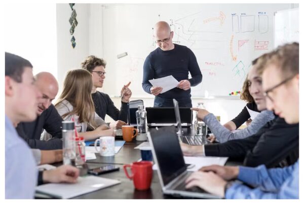Människor i samtal kring ett konferensbord med en writeboard i bakgrunden.